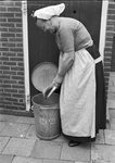 836319 Afbeelding van juffrouw Korving, bewoonster van het Meeuwenhofje te Scheveningen, die haar stofblik leeg klopt ...